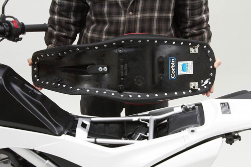 a person holding Dual Sport seat showing the back side, MPN printed and mounting brackets pre-installed