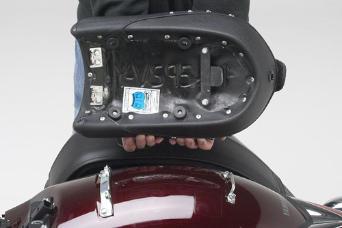 a person holding Touring Pillion seat showing the rear side, MPN printed and mounting brackets pre-installed