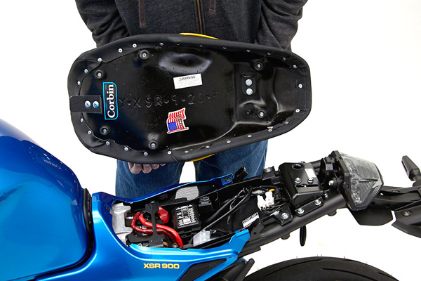 a person holding Gunfighter seat showing the rear side with MPN/Corbin sticker printed and mounting brackets pre-installed