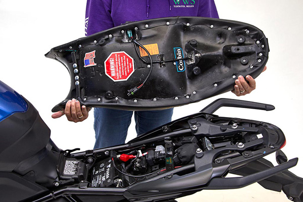 a person holding Canyon Dual Sport seat showing the rear side heater wiring with MPN printed and mounting brackets pre-installed