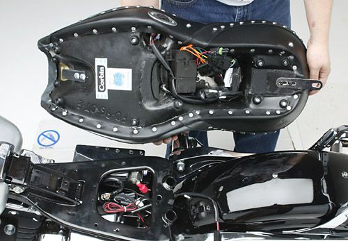 a person is holding Dual Tour seat showing rear side MPN printed, Heater wiring harness and mounting brackets pre-installed