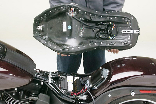 a person is holding Dual Touring seat showing rear side MPN printed, heater wiring and mounting brackets pre-installed