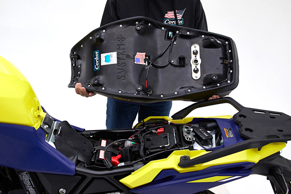 a person is holding Dual Sport seat showing rear side MPN printed, heater wiring harness and mounting brackets pre-installed