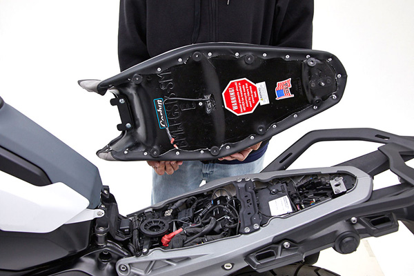 a person is holding Supermoto Seat showing back side, MPN printed, heater wiring and mounting brackets pre-installed